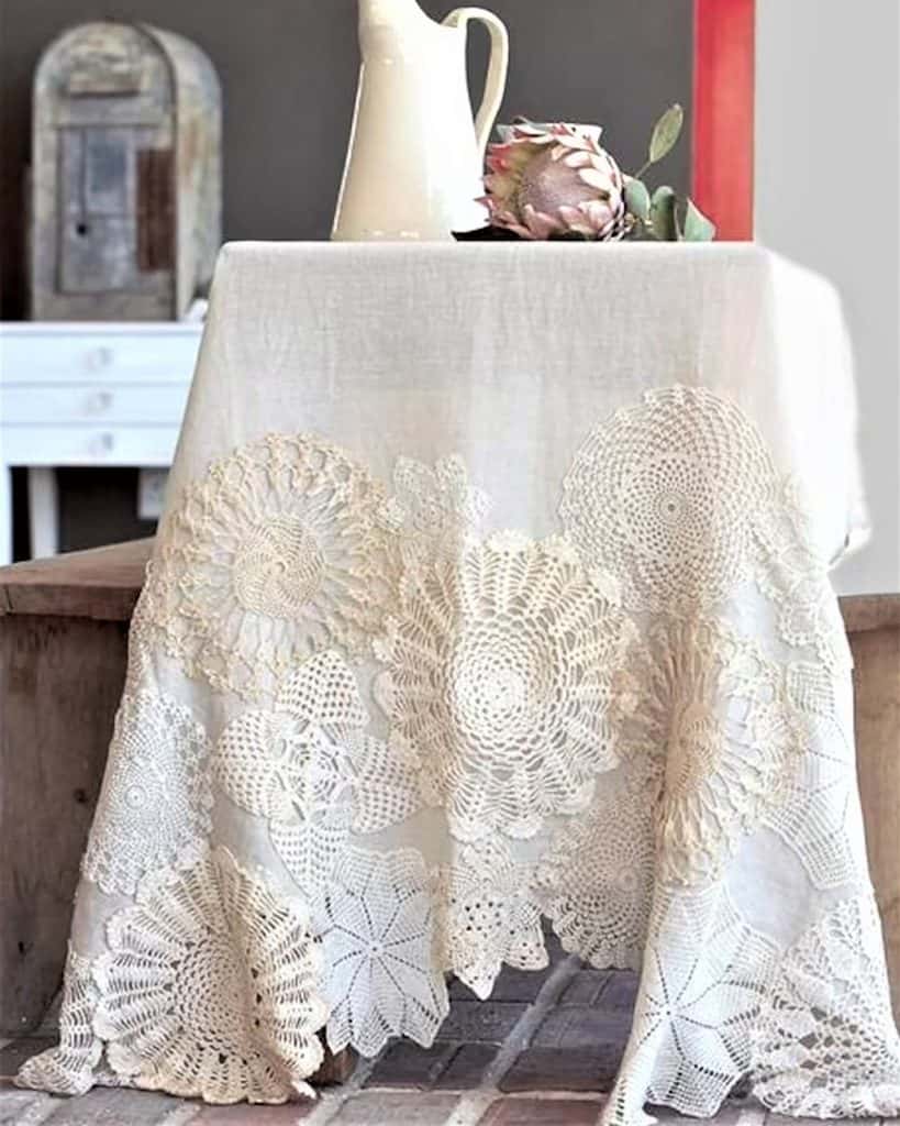 Decorative vintage doily tablecloth on a round table with a vase and flowers.
