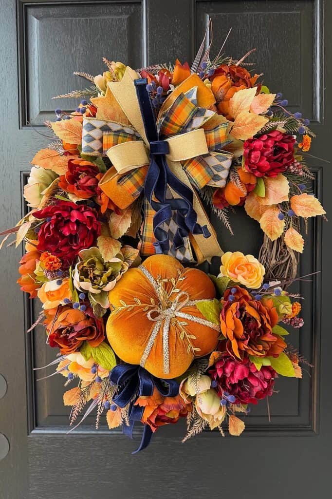 Autumn wreath with pumpkins, flowers, and plaid ribbons for fall decor.