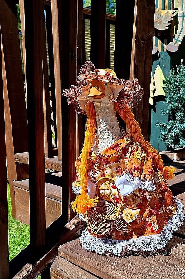 Decorative fall-themed goose with dress and basket on porch railing.