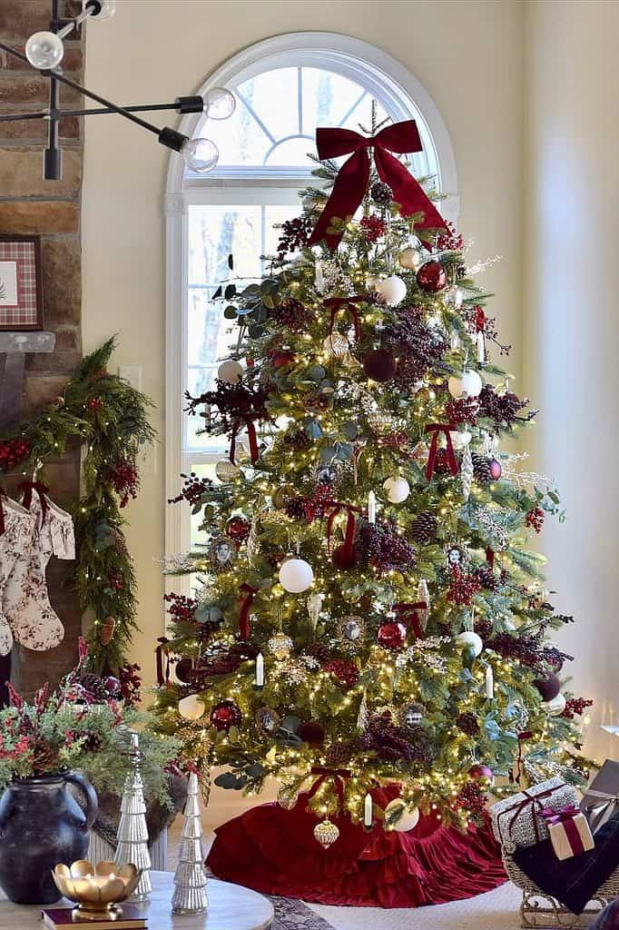 Beautiful decorated Christmas tree with red ribbons, ornaments, and lights in a cozy home.