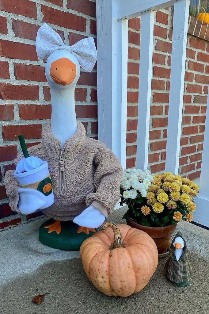 Decorative goose with pumpkin and flowers on a fall porch for autumn decor.