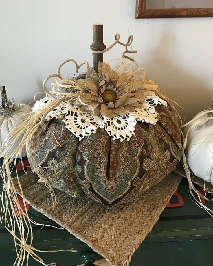 Fabric pumpkin decorated with doilies, flowers, and twine for fall decor.