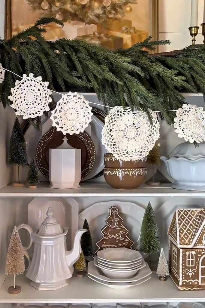 White crocheted doilies hanging on a Christmas garland with holiday decorations.