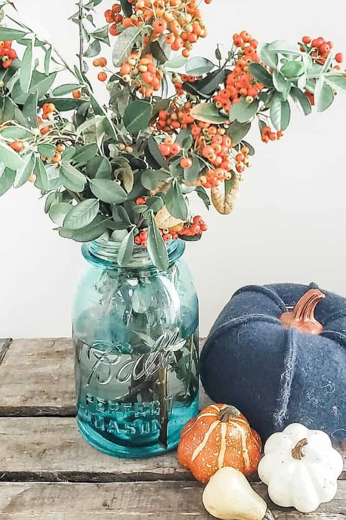 Autumn fall decor with pumpkins, berries, and a blue jar on wooden surface.