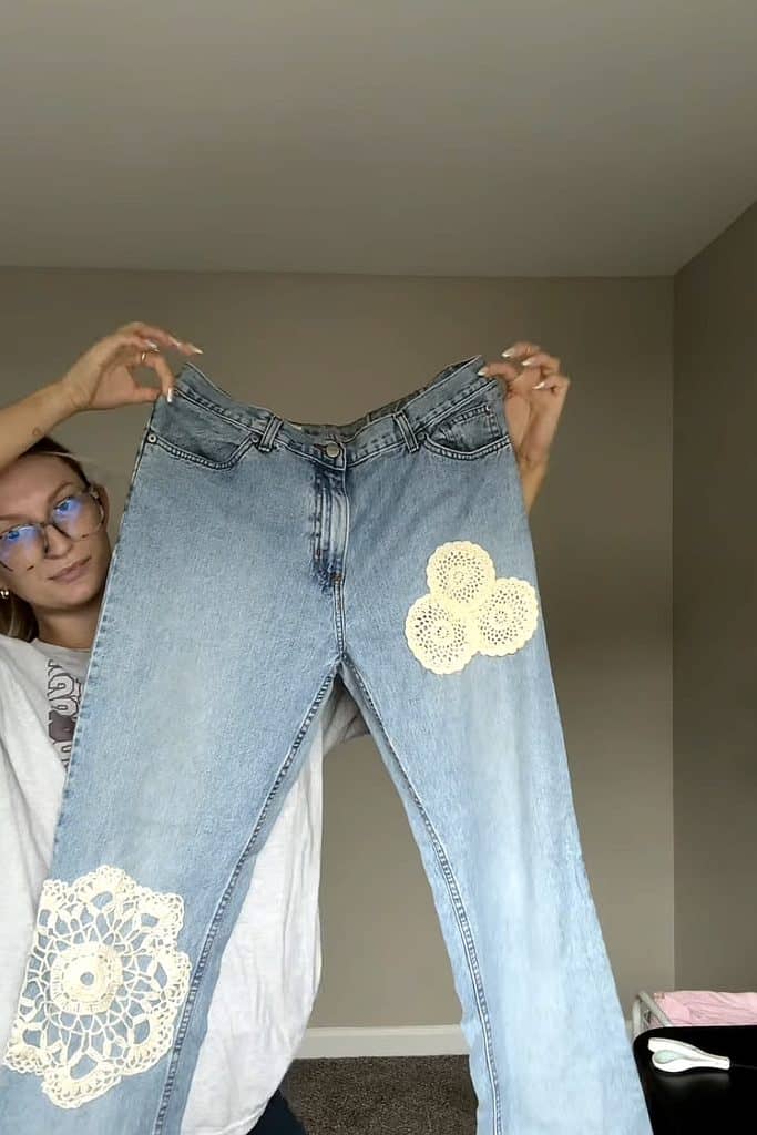 Denim jeans decorated with white doilies for creative reuse.