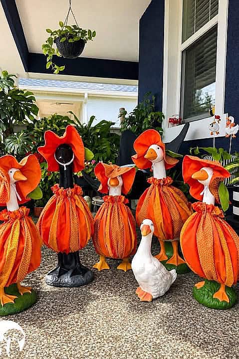 Colorful fall-themed goose decorations for porch decor with pumpkins and greenery.