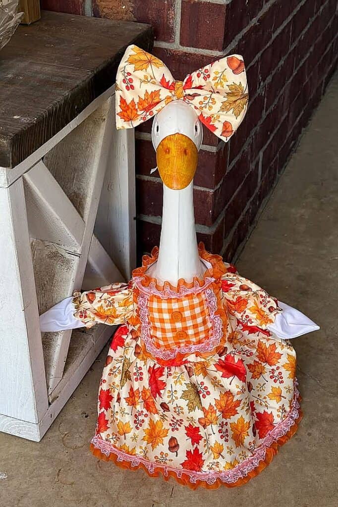 Decorative goose with fall leaves and gingham dress for autumn porch decor.