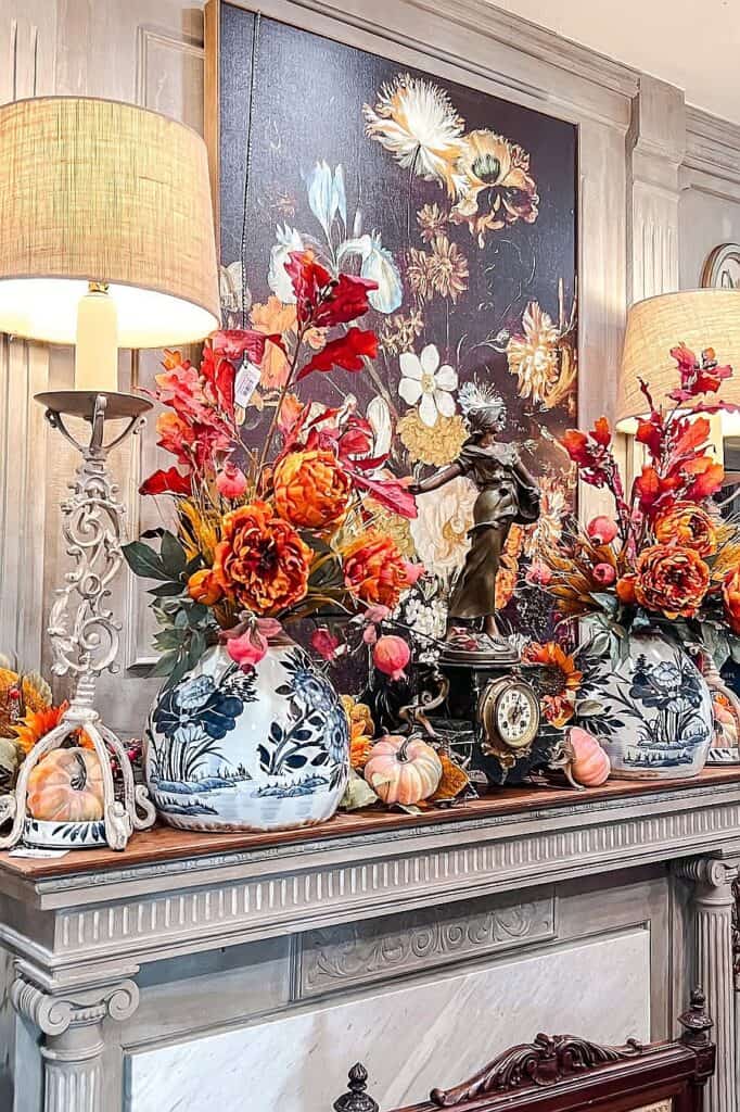 Fall floral decor with orange and red flowers in blue and white vases on a mantel.