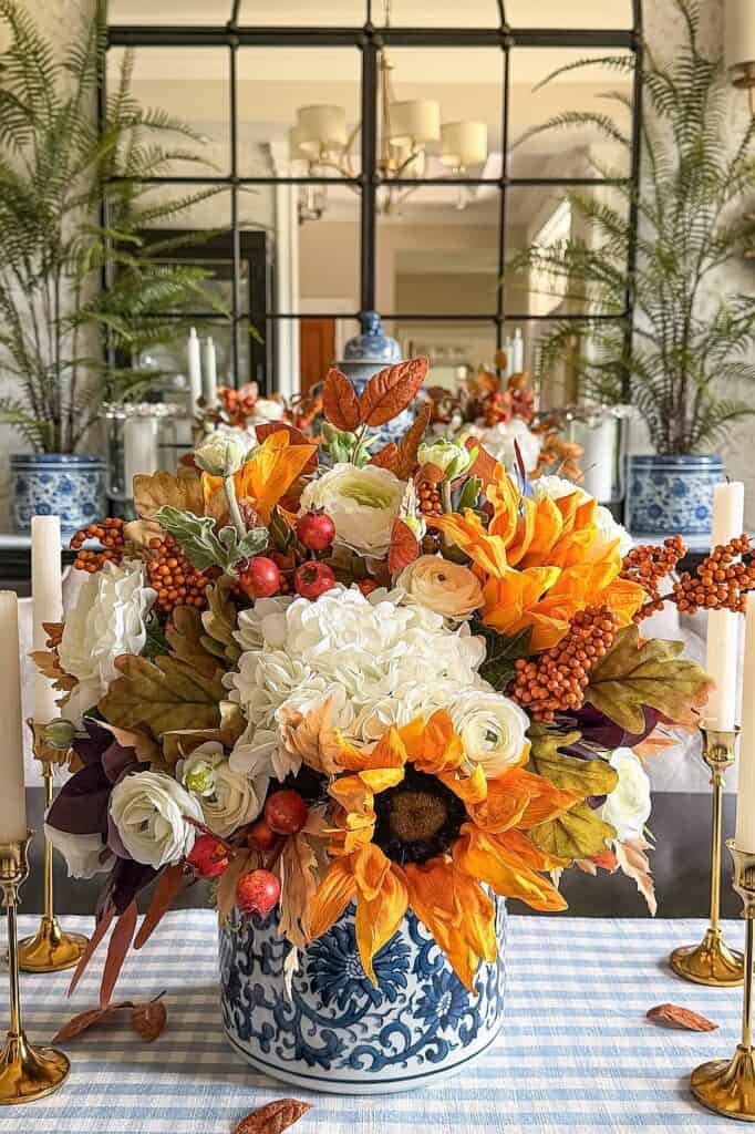 Colorful fall flowers with sunflowers, roses, and berries in a blue and white vase.