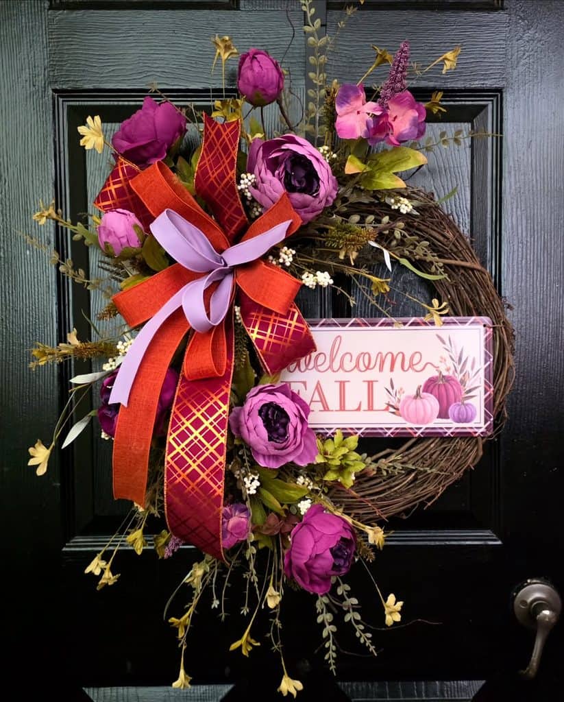 Decorative fall wreath with purple flowers, ribbons, and a welcome sign on a door.