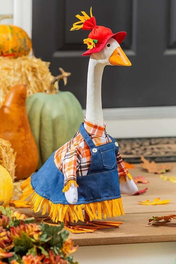Decorative goose dressed in fall-themed outfit with pumpkins and autumn leaves.