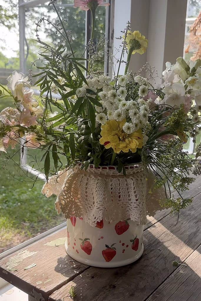 Beautiful fresh flower bouquet in a strawberry decorated jar on windowsill.