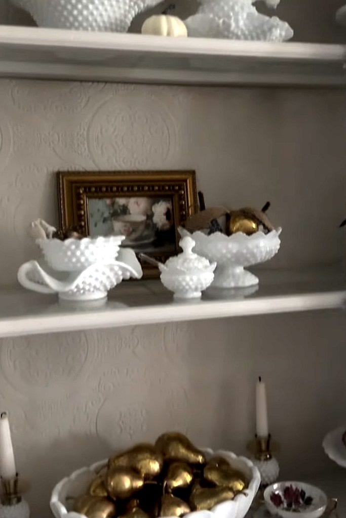 Elegant milk glass bowls and vases with gold accents on a shelf.