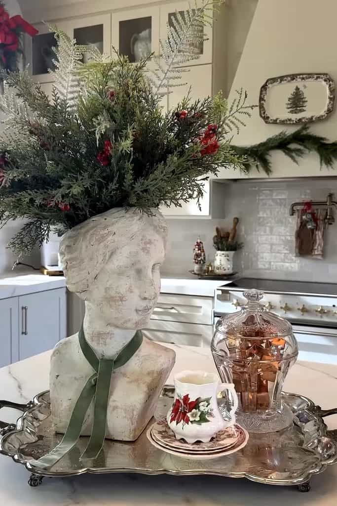 Festive Christmas decor featuring greenery, a bust, and silver tray with holiday items.