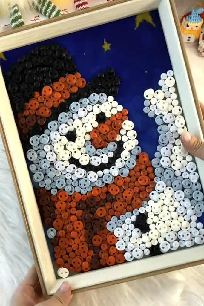 Colorful button snowman craft with a blue background and festive details.