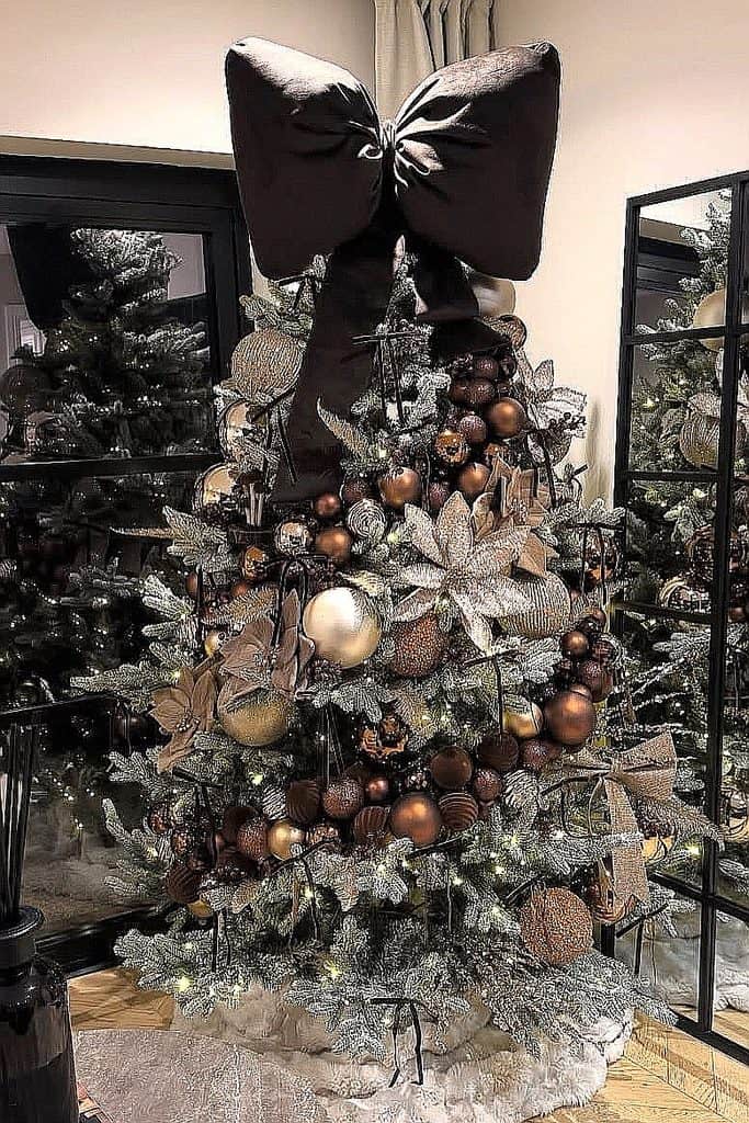 Elegant brown Christmas tree with ornaments and a large bow topper.