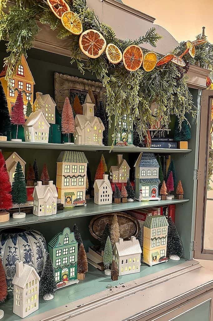 Festive Christmas village display with miniature houses and dried fruit garland.