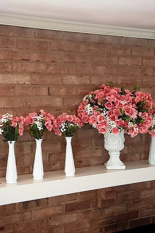 Beautiful pink and white floral display in milk glass vases on a white shelf.