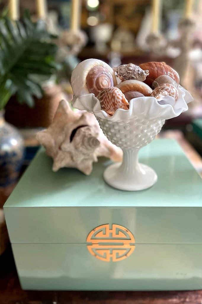 Decorative milk glass bowl filled with seashells on a pastel box.