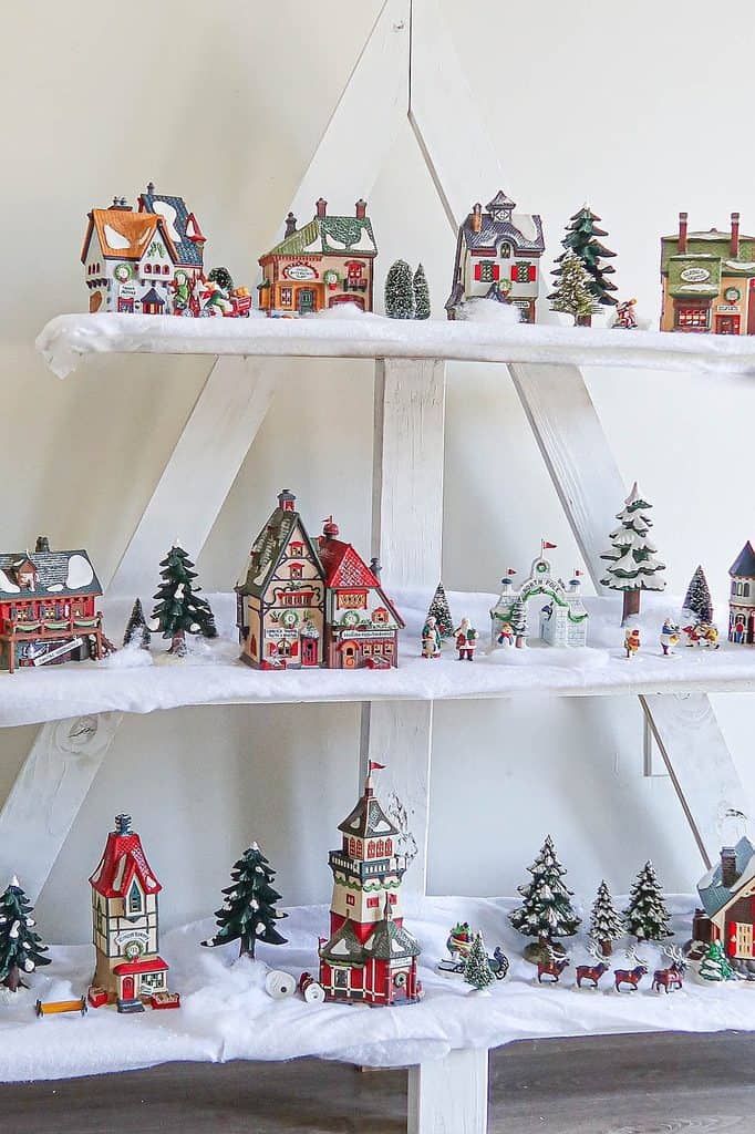 Festive Christmas village display with miniature houses and trees on snowy shelves.