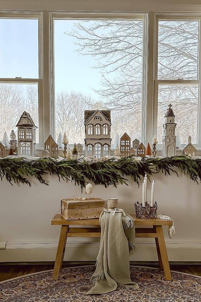 Festive Christmas village scene with miniature houses and trees on windowsill.