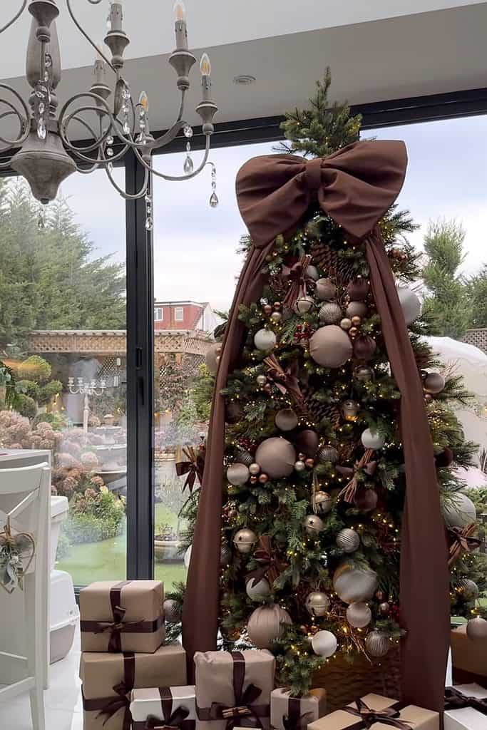 Decorated Christmas tree with a large bow and ornaments in a cozy indoor setting.