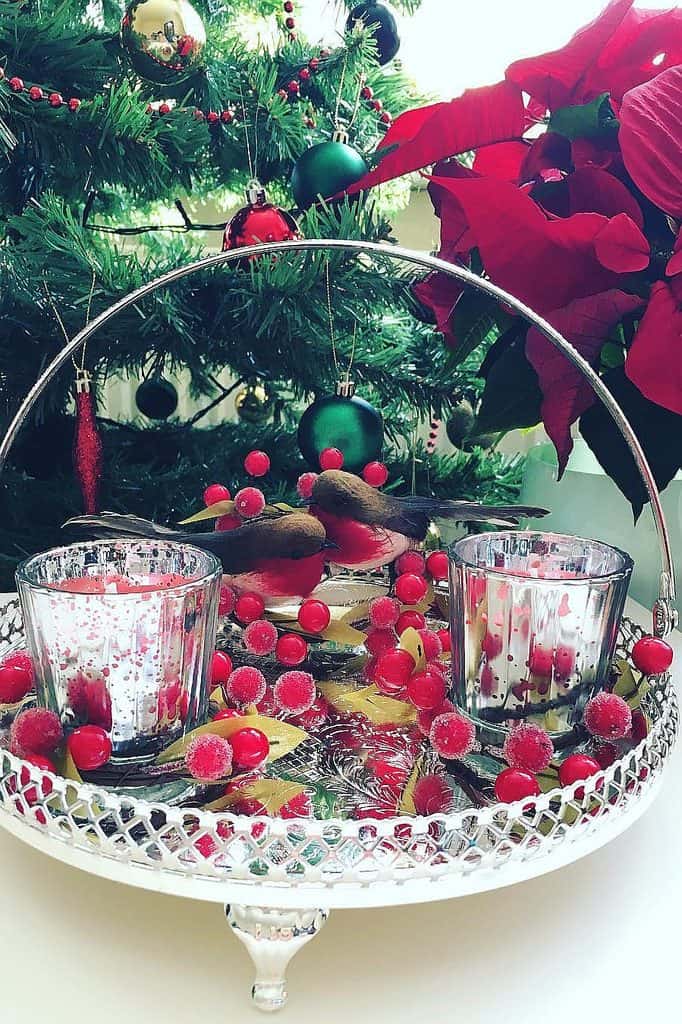 Elegant silver platter with red berries and candles under a Christmas tree.