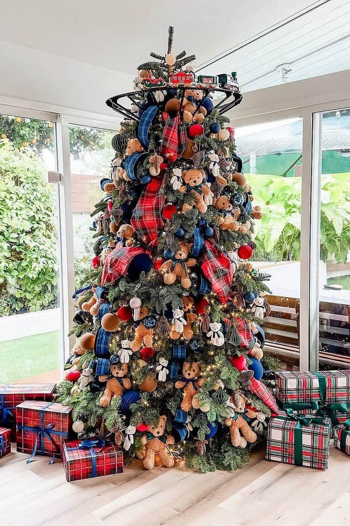 Decorated Christmas tree with teddy bears, plaid ribbons, and ornaments in a bright room.