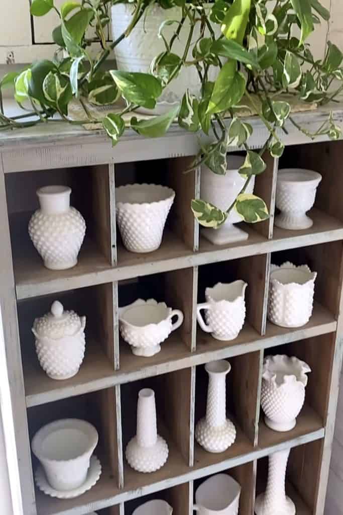 Charming milk glass collection displayed on a rustic wooden shelf with greenery.