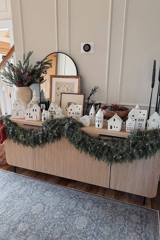 Festive Christmas village display with greenery and holiday decor.